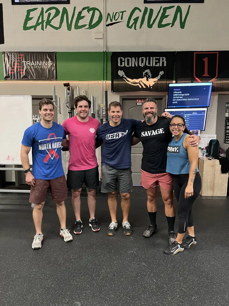 Five members standing arm-in-arm together after a workout in front of an Earned Not Given wall mural.