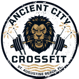 Ancient City CrossFit badge logo: a roaring lion biting a barbell, flanked by palm trees, ringed with St. Augustine Beach, FL.